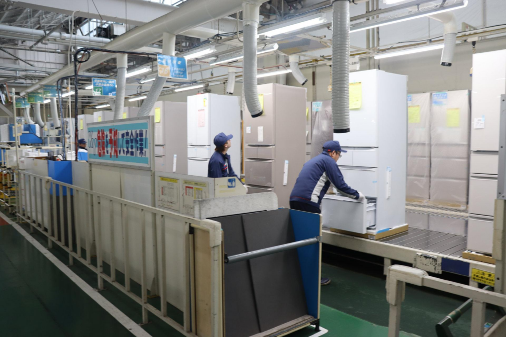 Trabajador inspeccionando un refrigerador en una fábrica antes del embalaje y envío